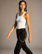 A woman modeling a white ribbed tank top and black jeans with a silver wallet chain accessory hanging from the pocket, posed against a neutral gray studio background.