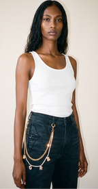 A woman modeling a white ribbed tank top and dark jeans, accessorized with a gold wallet chain belt featuring letter charms, spelling out bee great